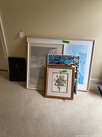 Grouped view of five framed artworks leaning against wall, showing floral painting, rainforest poster, blue-toned and monochrome artworks.