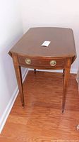 Full view of the Baker Furniture drop leaf side table showing the front with dovetail drawer and brass round handles, decorative inlay on legs, and caster wheels.