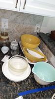 Overview of glassware, ceramic bowls including yellow bowls, speckled bowl, turquoise interior bowl, rectangular white platter on countertop