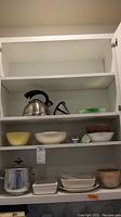 Overall view of cabinet shelves with kettle, bowls, and dishes
