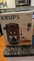 Front of the Krups Bravo Plus espresso machine box showing the machine and steam nozzle, with coffee cup illustrations.