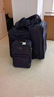 Five pieces of luggage stacked together on carpeted floor, various sizes from small to large.