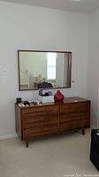 Straight-on view of the wooden framed mirror hanging above a dresser, showing size and style in a living space.