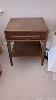 Front view of wooden nightstand showing a rectangular top, single drawer with slim handle, tapered legs, and lower shelf.