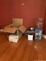 Wide view of lot items including boxed small appliances, glass punch bowl, Dansk vase and coasters, and Profiles beer mugs.