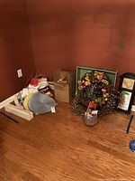 Wide view showing assorted linens, wreaths, wallpaper boxes, and wall mirror grouped on the floor in a corner.