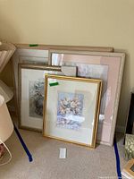 Four framed floral themed art pieces stacked and leaning against a wall.