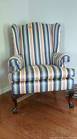 Front view of wing back chair showing striped fabric upholstery, wing back design, and carved claw and ball foot legs.