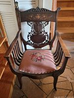 Front view of antique wooden armchair showing carved backrest, floral inlay on the upper panel, and needlepoint floral upholstered seat.