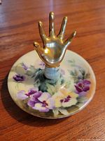 Photo showing the full ring holder with gold metallic hand and floral decorated base on wooden surface.