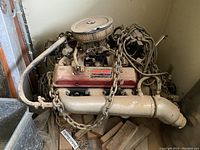 Overall view of the Chevrolet small-block V8 engine with red Trans-Dapt valve covers, metal intake manifold, carburetor, round air cleaner, and lifting chains