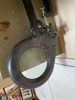 Close-up of large circular glass lens with black metal frame and part of articulated arm.