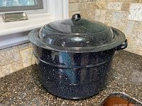 Black graniteware canning pot with lid on, showing the speckled white pattern and sturdy handles