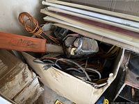 Wide view showing Stihl chainsaw with orange bar cover inside cardboard box along with several extension cords coiled around.
