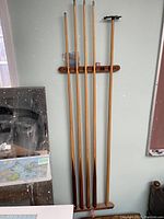 Four wooden pool cues and a wooden cue rack mounted on a wall, showing full length of cues.