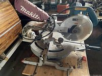 Front perspective of Makita LS1013 sliding compound miter saw mounted on wooden support with dust bag attached