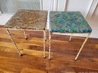 Pair of vintage stools with metal twisted legs and square floral vinyl seats in brown and blue colors, placed on wood flooring.