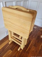 Front view showing four folded wooden folding tables held together in a wooden carrier/holder with a handle.