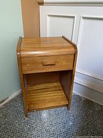 Front angle view of wooden side table showing drawer and lower slatted shelf.