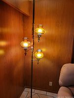 Full view of the vintage floor lamp standing in a corner showing the three lit amber glass fixtures and wooden pole.