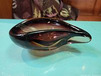 Side view of the vintage art glass bowl showing its curved, pointed teardrop shape and amber to dark brown gradient color.