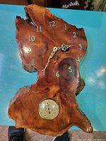 Vintage burlwood wall clock with brass numbers and inset thermometer placed on blue surface.