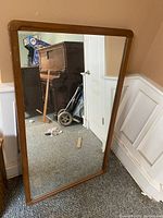 Full view of the rectangular vintage mid-century modern mirror leaning against a wall, showing the walnut wood frame and reflective surface.