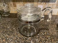 Front view showing entire Pyrex glass coffee percolator carafe with handle and lid on black granite countertop.
