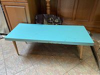 Full view of the turquoise Arborite coffee table showing rectangular top and wooden legs.