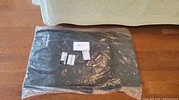 Two black Mercedes Benz AMG front floor mats in original clear packaging placed on wooden floor.