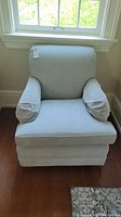Front view of the pale green upholstered armchair with cushions and armrests.