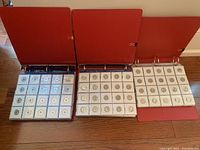 Three red binders open on floor showing pages of coin flips holding assorted coins