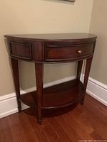 Front view of demi-lune table showing curved top, drawer, and lower shelf