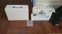 Kenmore sewing machine with carrying case and bag of bobbins on hardwood floor