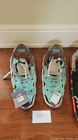 Pair of mint green Tubbs Frontier 21 women's snowshoes placed on a hardwood floor, showing both snowshoes and the involved bindings, with tags still attached.