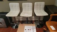 Three assembled white vinyl adjustable stools with chrome bases and one unopened box on hardwood floor