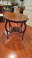 Front angle view of the round scalloped edge antique wood table showing carved legs and lower shelf.