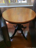 Front view of the round accent table showing the wooden top and black base between two chairs.