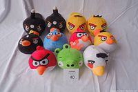 Photo showing 7 Angry Birds plush toys including black bomb birds, yellow birds, red birds, blue bird, green pig, and white bird on a white background.