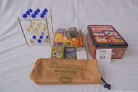 Front view of the three children's games displayed together: Marble 3D Tic Tac Toe on left, Safari Rush Hour pieces in middle, Sushi Go Party! tin box on right and Safari Rush Hour drawstring bag in front.