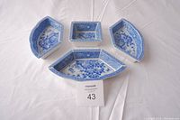 Set of four blue and white porcelain dishes arranged on a white surface, showing shape and size variety.