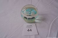 Side view of the clear glass paperweight showing the blue flower and bubble details inside.