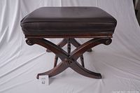 Front view of the stool showing the leather seat and wooden X-shaped cross legs with circular carved details at intersections.