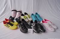 Photo showing all cleats and shin guards in lot, including Mitre yellow youth cleats, Nike black cleats, Adidas black cleats, Adidas shin guards, Puma running shoes white pink, Columbia running shoes, Nike running shoes.