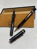 Two black pens with gold accents placed in original box, one with cap removed and one capped pen.