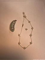 Photo of the jade and pearl pendant alongside the pearl-accented necklace on a plain background.