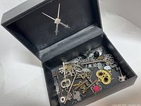Opened black leather jewelry box with silver crossed swords showing assorted skeleton keys inside.