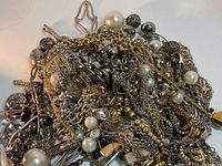 Tangled pile of mixed gold-tone and silver-tone chains with pearl and metallic bead details, showing cross and metallic pendants.