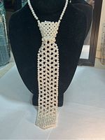 Front view of a long white pearled necklace styled to look like a necktie with a wide knot and a long rectangular tail section.