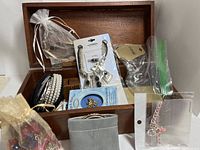 Dark brown wooden box, 18 inches, filled with multiple assorted jewelry items including prepackaged necklace and earring sets, small organza bags with jewelry, and various loose costume jewelry pieces.